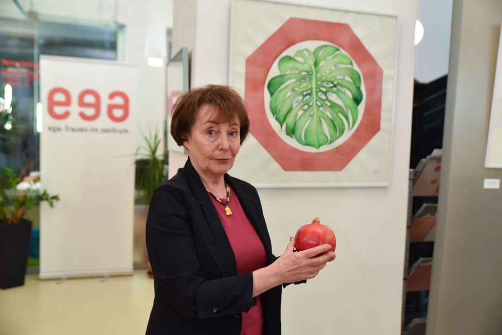 Nina Werzhbinskaja-Rabinowich mit einem Granatapfel in der Hand vor ihrem Bild „Ein Blatt namens Argus“